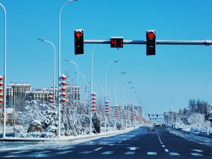 A quiet winter street in Tianjin, China, with snow-covered lanterns and traffic lights.
