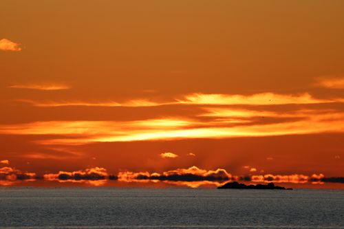 Free Dramatic sunset with vibrant orange sky and silhouetted horizon over a calm ocean. Stock Photo