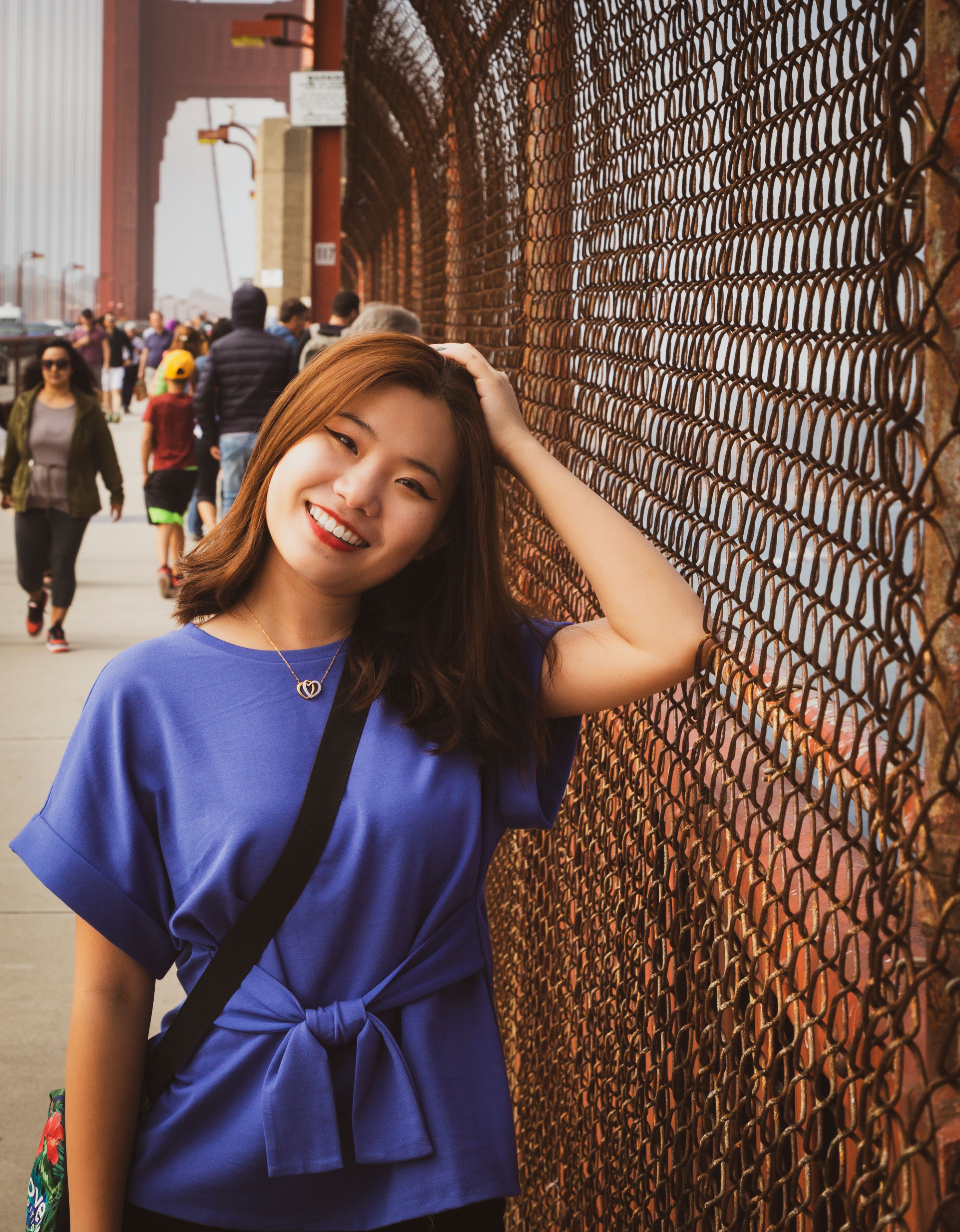 A young woman smiles while posing by a fence near the Golden Gate Bridge in San Francisco.