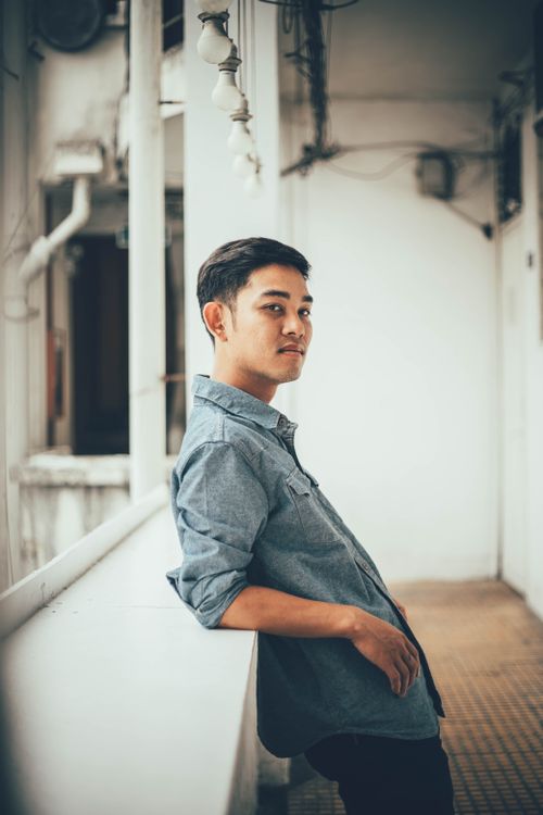 Free A relaxed portrait of a young man leaning against a railing indoors with a thoughtful expression. Stock Photo
