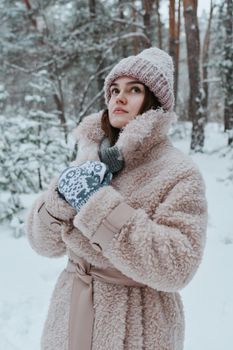 Woman in winter attire posing in a snowy forest, showcasing cozy fashion.