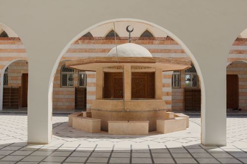 Free Elegant mosque courtyard featuring an arched doorway and a central stone fountain under sunny daylight. Stock Photo