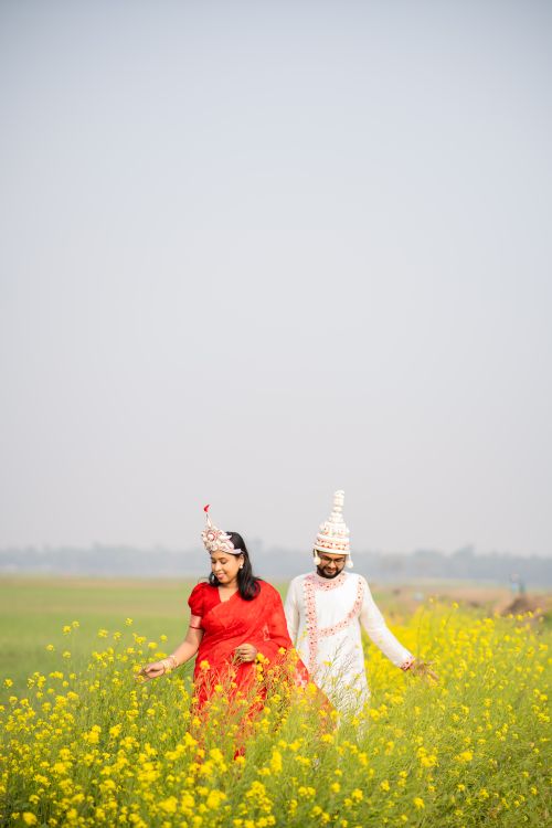 Free Bride and groom in traditional attire walking through a scenic mustard field in Kolkata. Stock Photo