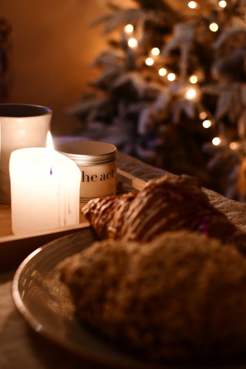 Free Warm, intimate holiday scene with candle, pastries, and Christmas tree lights. Stock Photo