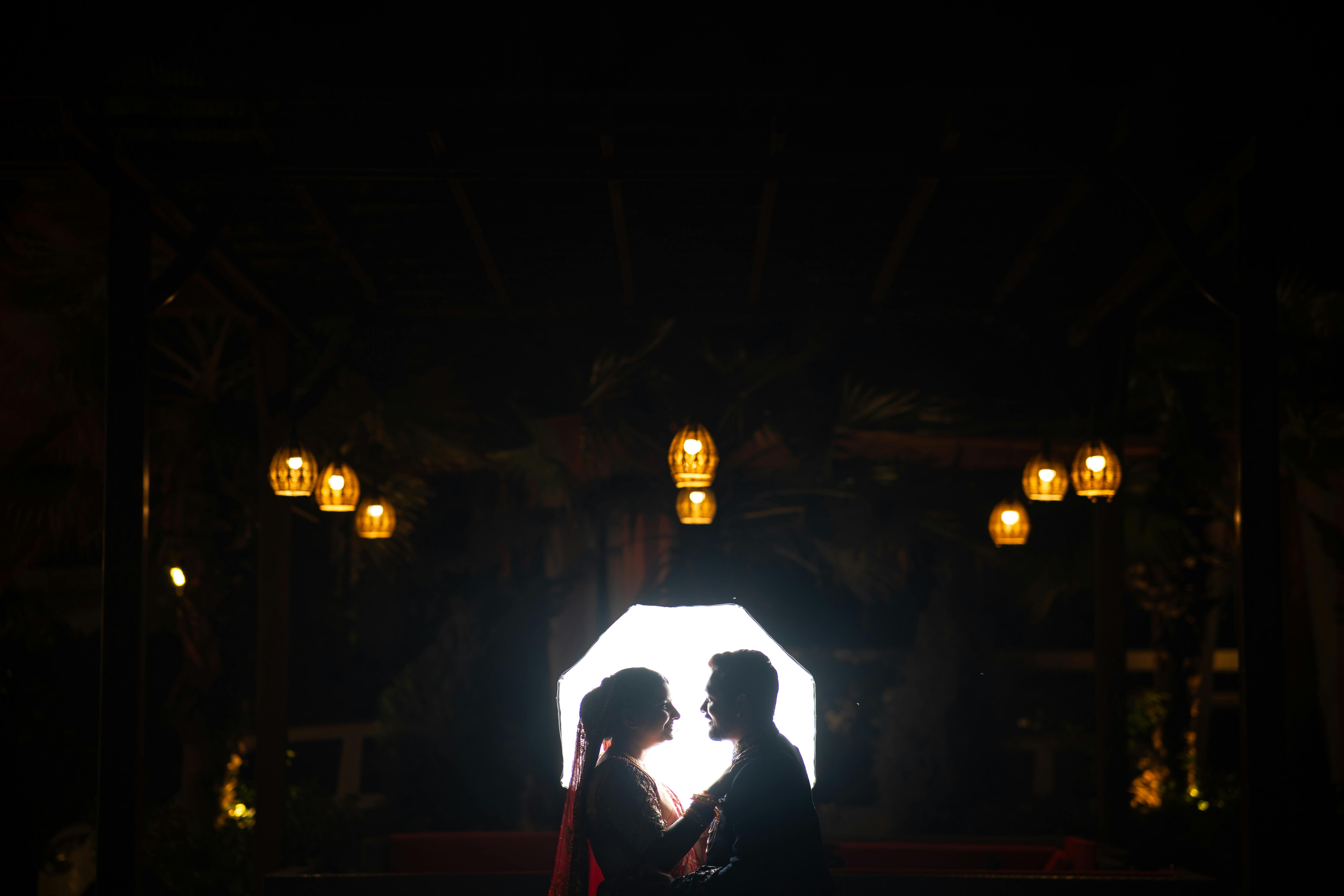 Silhouetted couple in a romantic embrace under rustic lantern lights at night.