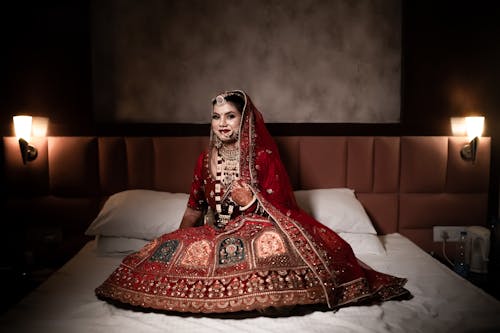 Elegant Indian Bride Sitting on a Bed in Traditional Wedding Clothing 