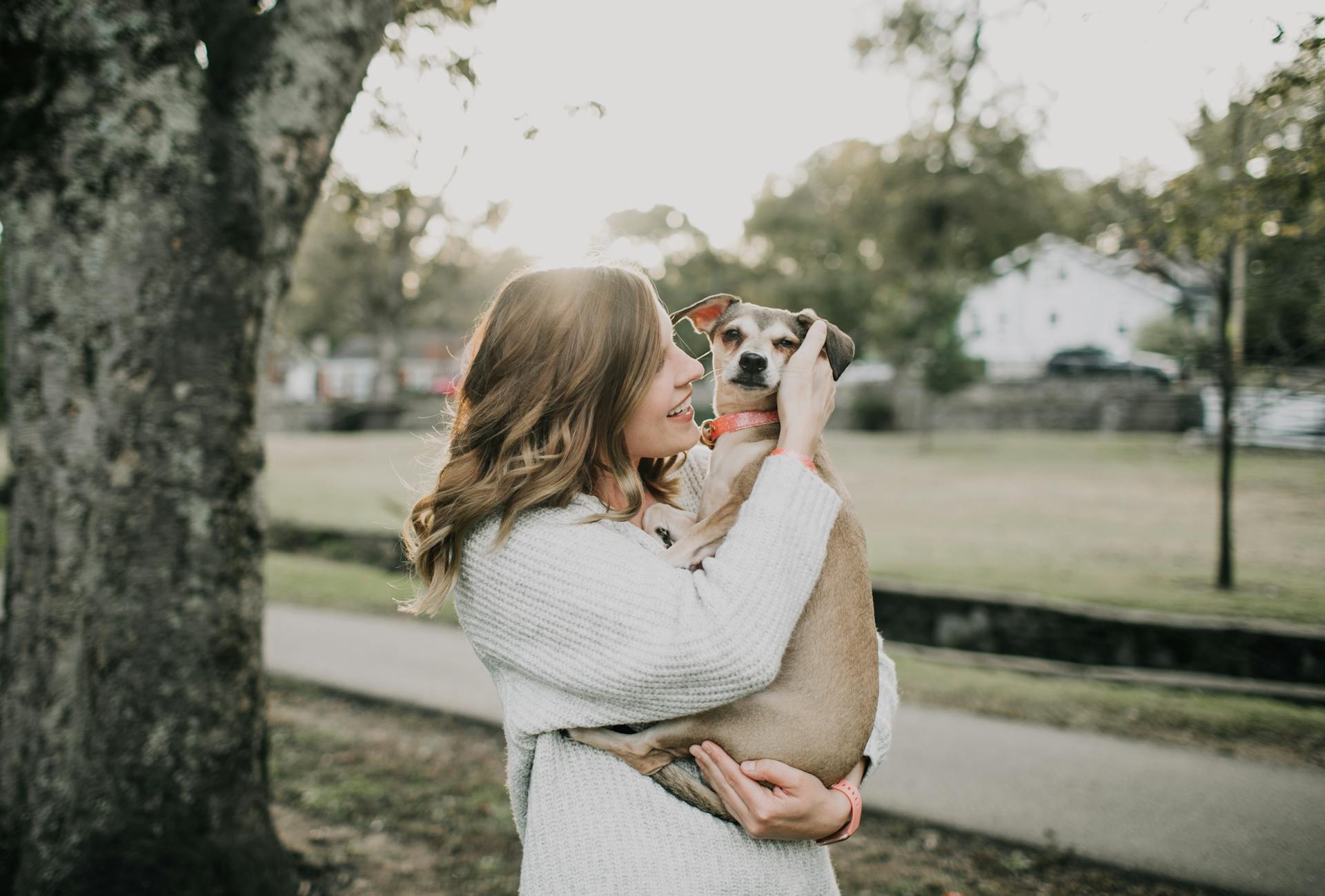 Une femme souriante porte un chien près d'un arbre