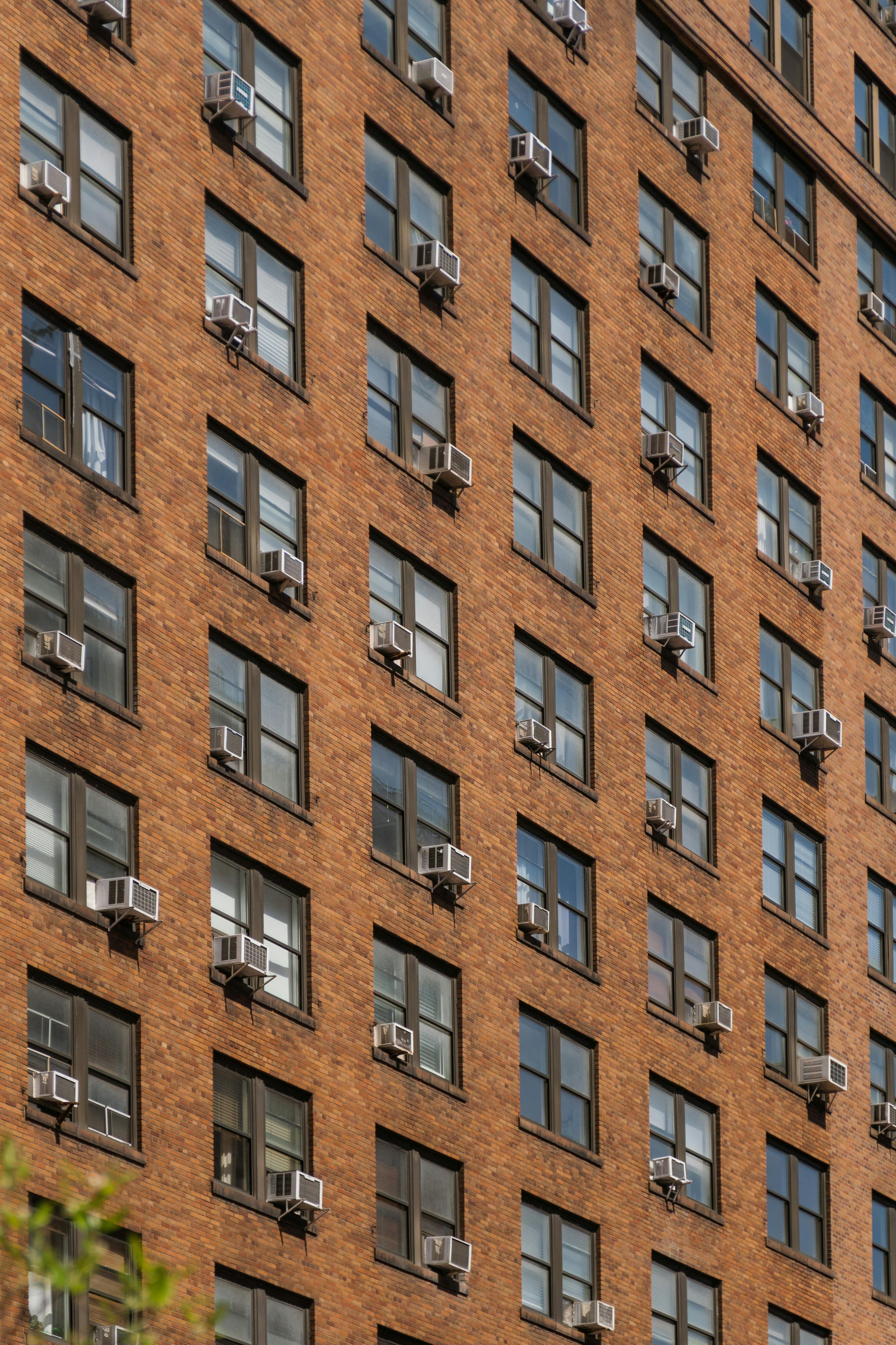 Close-up of a brick residential building with numerous windows and air conditioners.