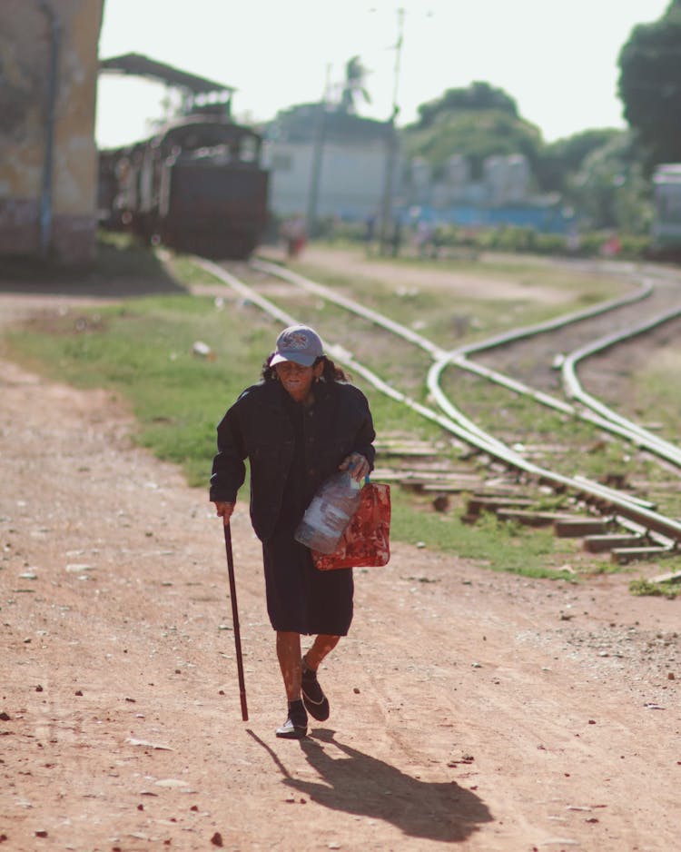 Elderly Woman With Walking Stick Carrying Plastic Bottle