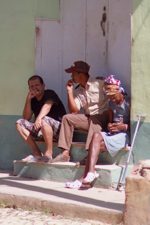 Free Three adults sitting on steps, conversing and relaxing in urban sunlight. Stock Photo