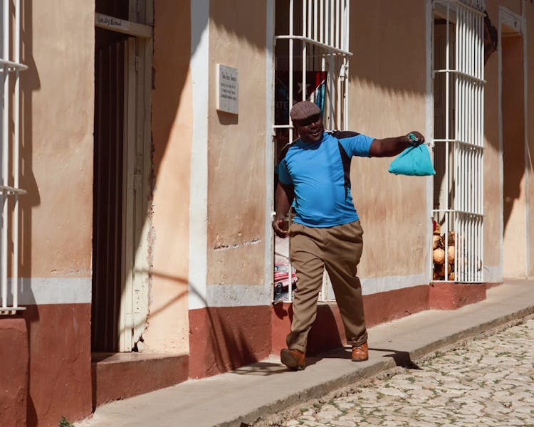 Man Walking On The Sidewalk And Holding A Blue Sack 