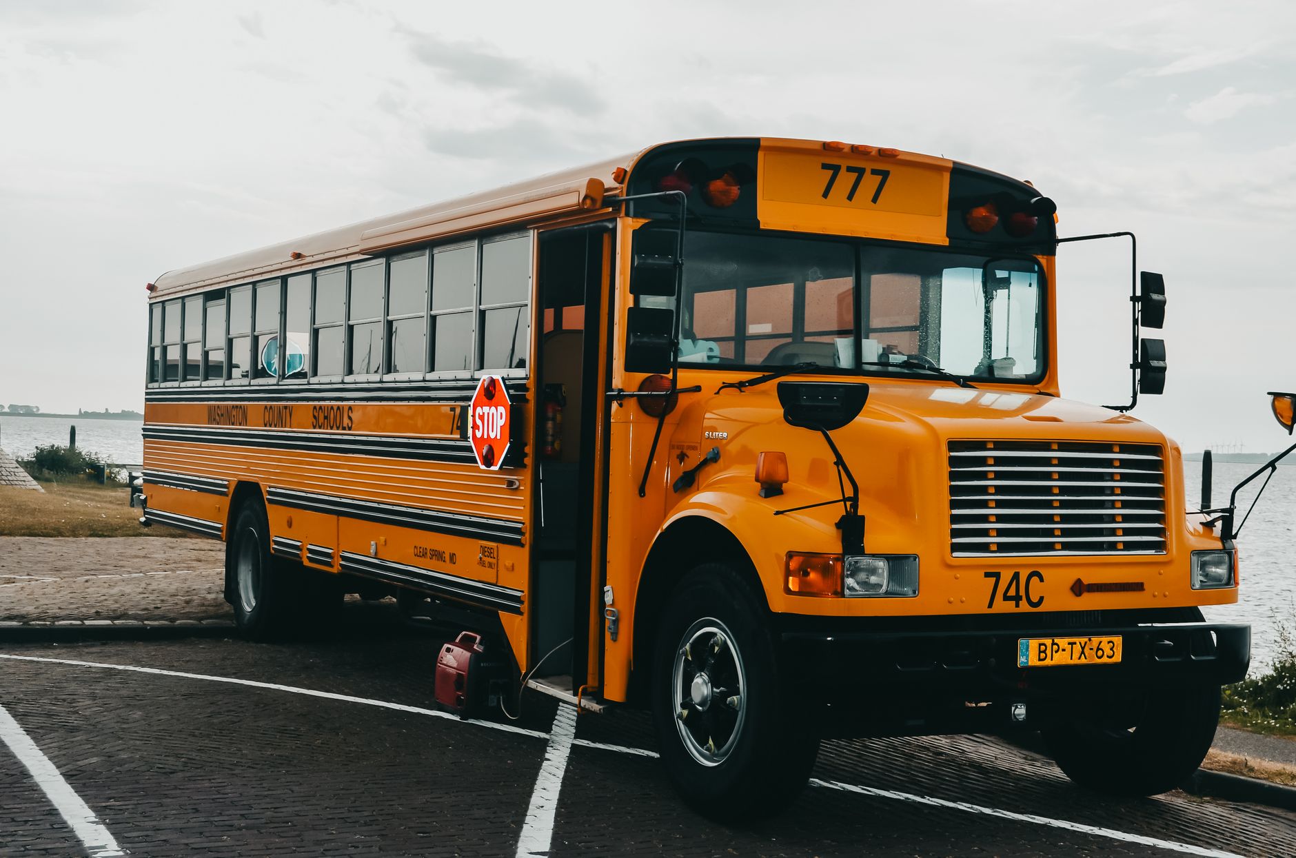 Classic American yellow school bus parked by a serene lakeside in an urban setting.