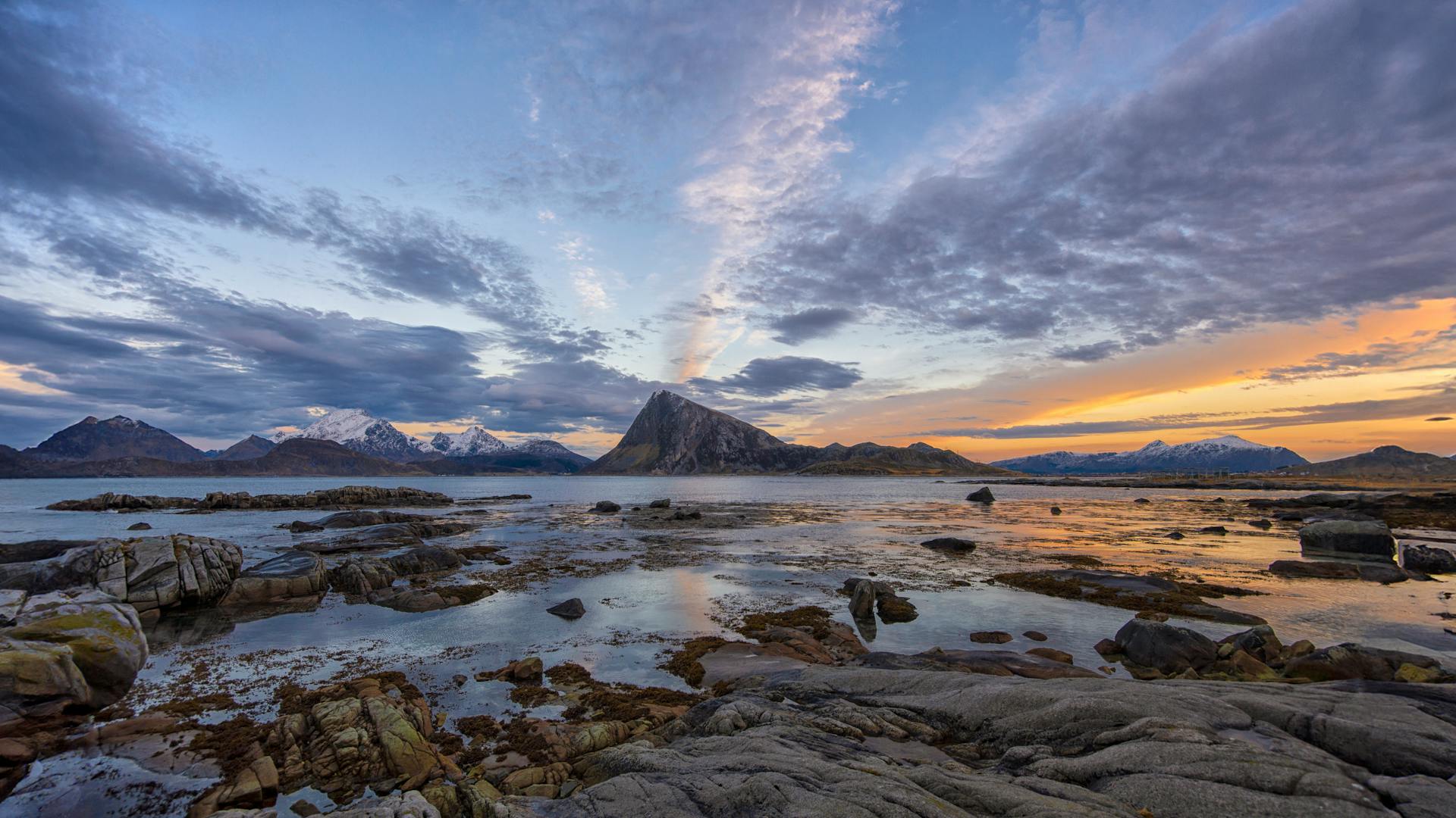 Breathtaking sunset over rugged coastal landscape in Norway with snow-capped mountains.