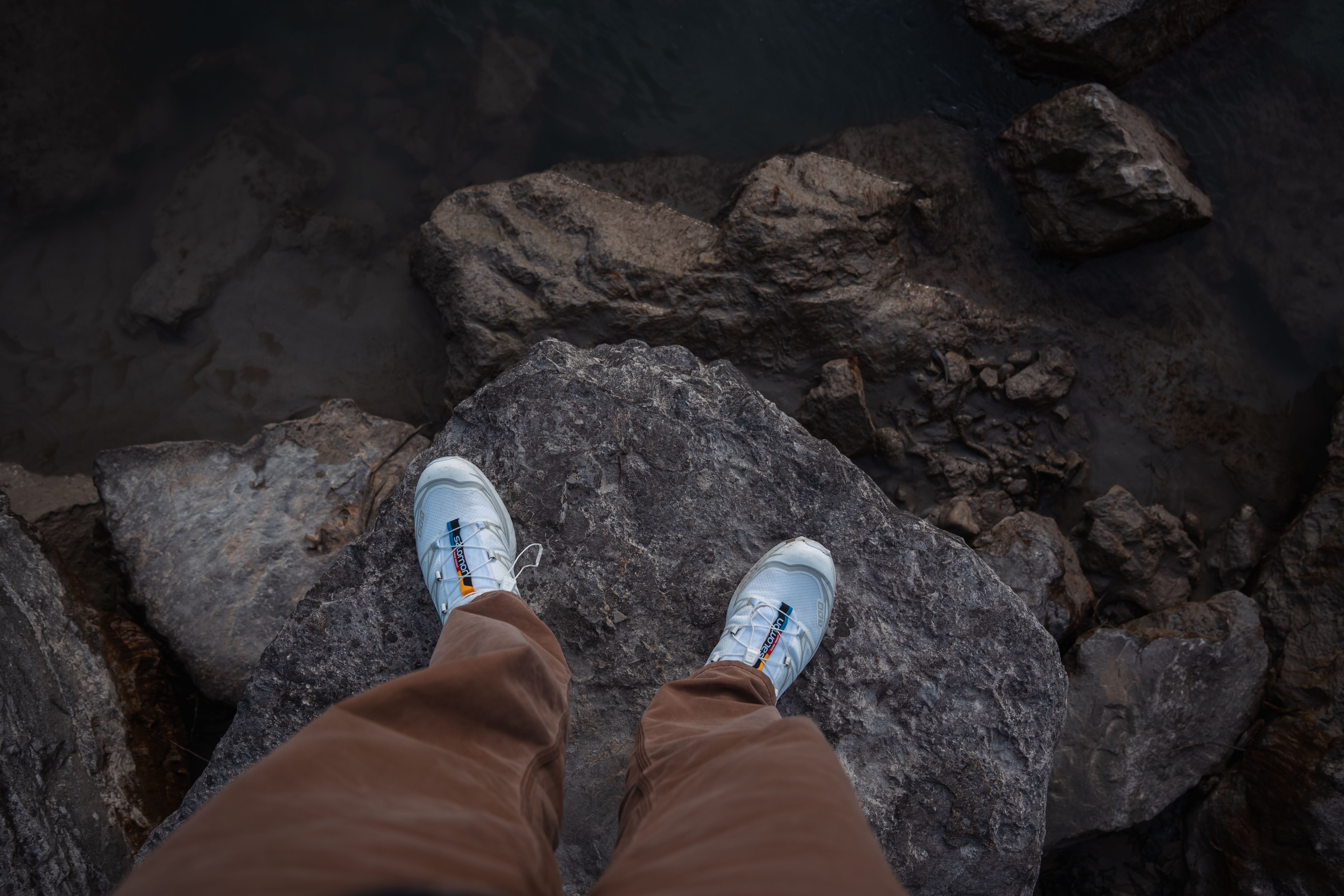 Top-down view of man’s sneakers on a rocky cliff edge, showcasing outdoor footwear style.