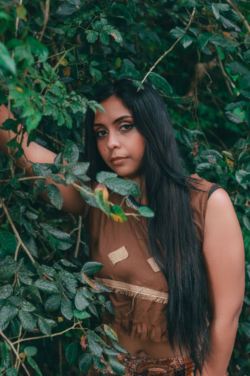 Free A woman with long dark hair stands amidst lush greenery, blending with nature's beauty. Stock Photo