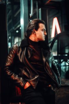 Portrait of a man in a black leather jacket posing on city streets at night.