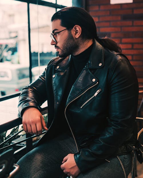 Bearded Man with Long Hair Wearing a Leather Jacket Sitting at the Table in a Cafe
