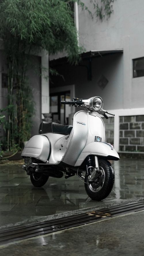 Free Vintage Vespa scooter parked on wet city street, capturing a nostalgic urban vibe. Stock Photo