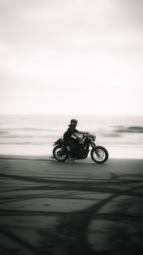 Free A lone motorcyclist rides across the beach in a striking black and white photo. Stock Photo