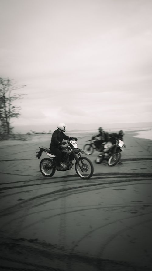 Free Three people riding motorcycles on the beach, captured in a black and white style. Stock Photo