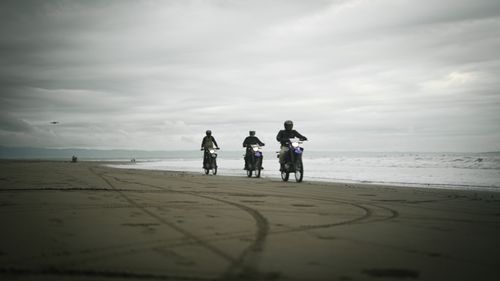 Free Three bikers ride motorcycles on a gloomy beach with overcast skies. Stock Photo