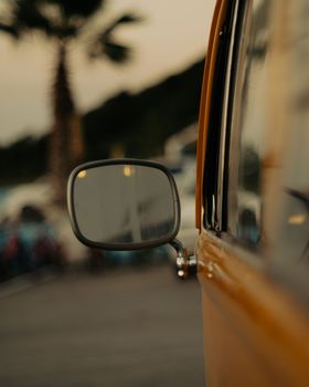 Close-up of a vintage car mirror reflecting an urban scene during sunset.