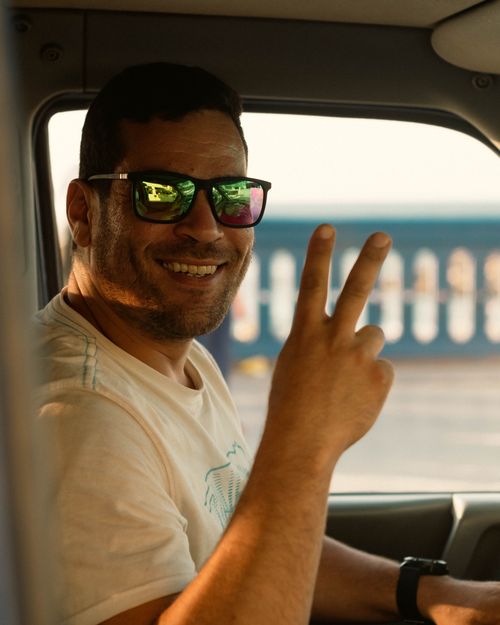 Free Happy man wearing sunglasses, smiling, and showing a peace sign inside a car. Stock Photo