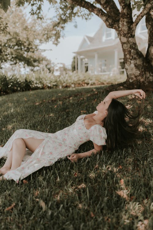 Young Woman in a Floral Dress Lying on the Grass in the Garden 