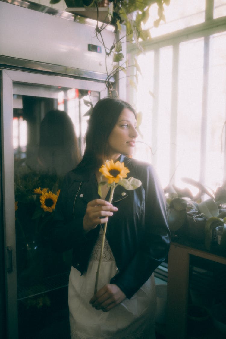 Young Woman Standing In A Room By The Window And Holding A Sunflower 