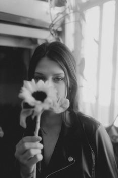 Black and white portrait of a woman in a leather jacket holding a sunflower.