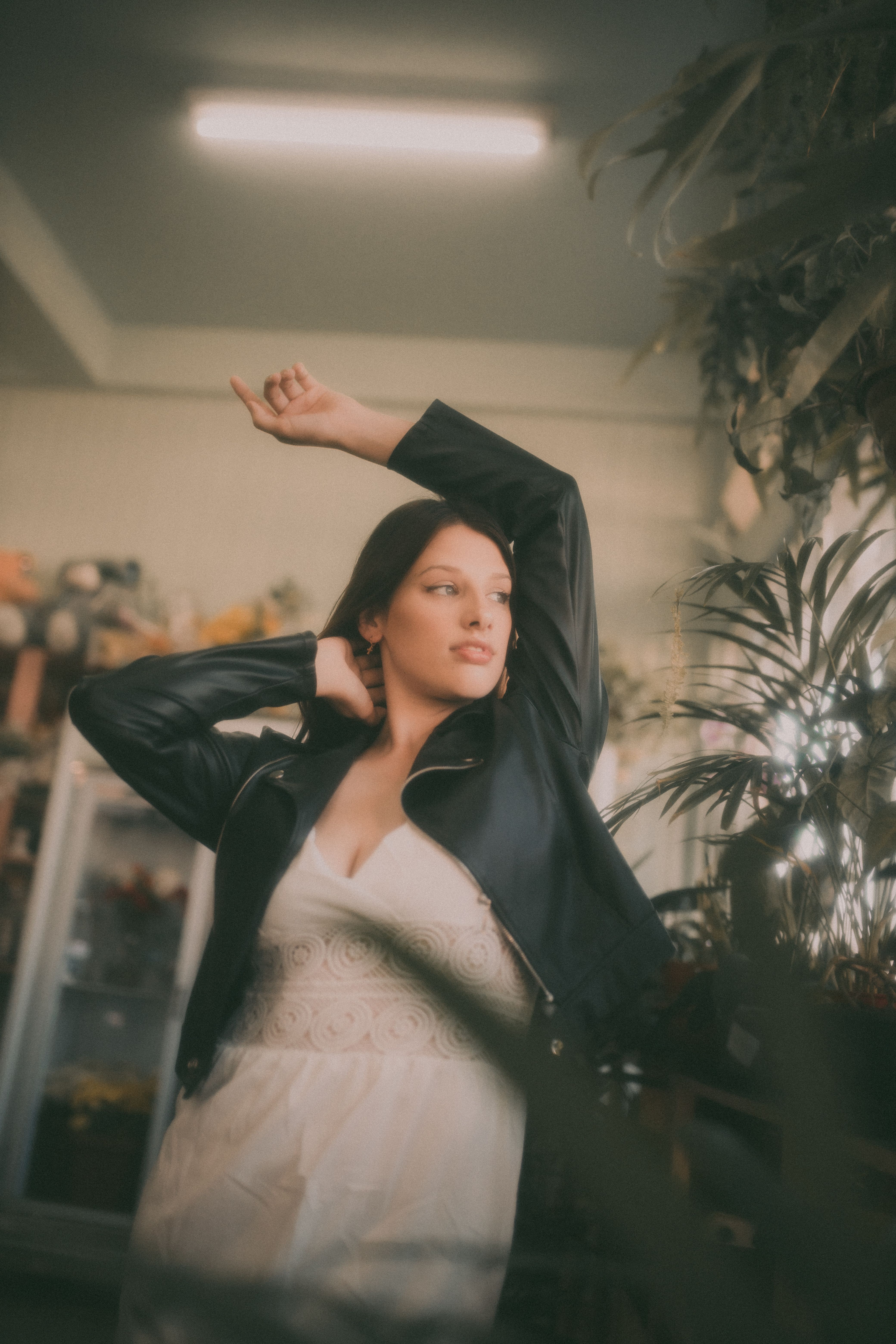 Stylish woman poses in a leather jacket and dress among indoor plants.