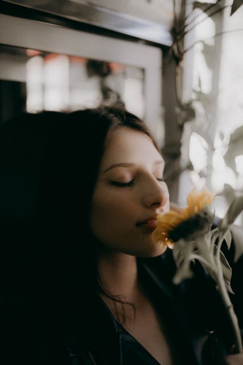Free Profile portrait of a woman with closed eyes, savoring the aroma of a sunflower indoors. Stock Photo