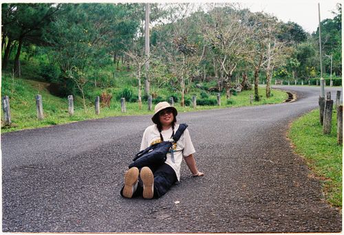 Free A woman sitting on a rural road surrounded by greenery, enjoying nature. Stock Photo