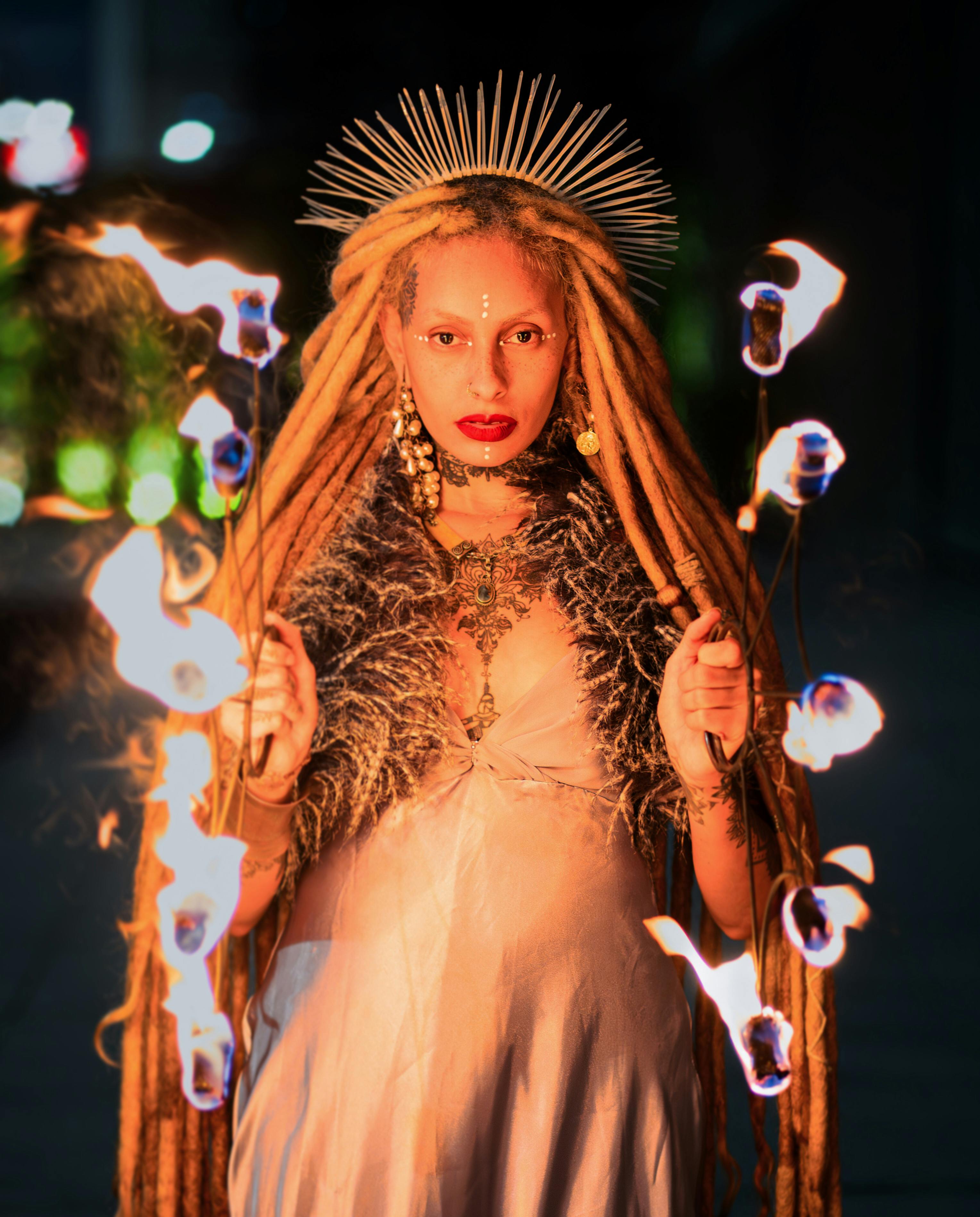 A captivating fire performer with long dreadlocks and a striking headpiece creates a magical scene.