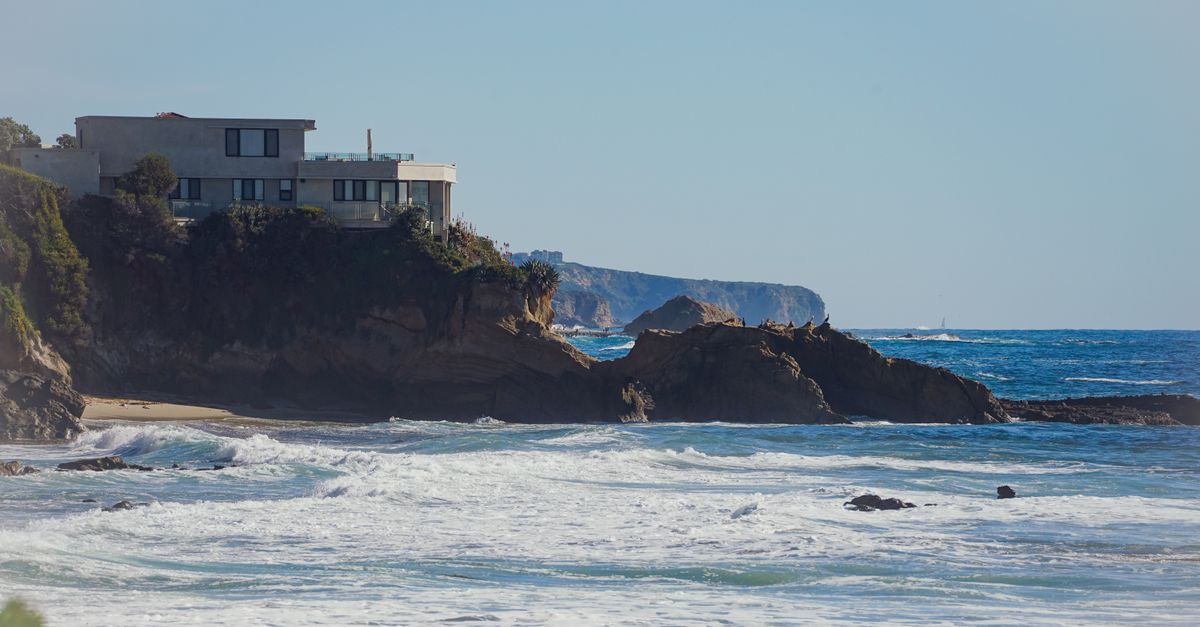 A stunning architectural house perched on a cliff with a breathtaking ocean view under a clear sky.
