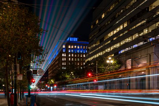 Illuminated city street at night with colorful light trails and skyscrapers.
