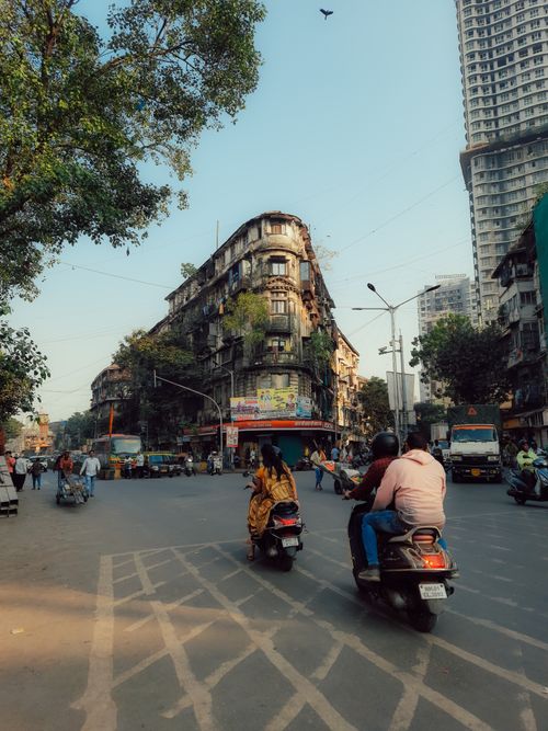 Free A lively street in Mumbai featuring scooters, old buildings, and urban life on a sunny day. Stock Photo