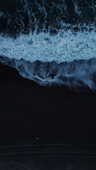 A stunning aerial photograph of waves crashing on a dark sandy beach at night.