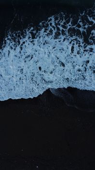 A mesmerizing aerial shot of ocean waves crashing onto a dark shore at night, captured from above.