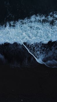 A captivating aerial shot of ocean waves crashing onto a dark sandy beach under the night sky.