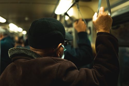 Free Man holding onto a subway handle, wearing a face mask, amidst a crowd. Stock Photo
