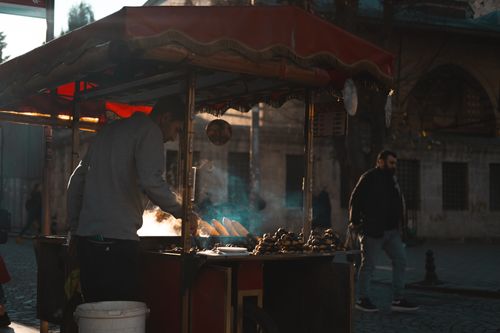 Free A street vendor cooks corn on a cart while steam rises in a bustling city environment. Stock Photo