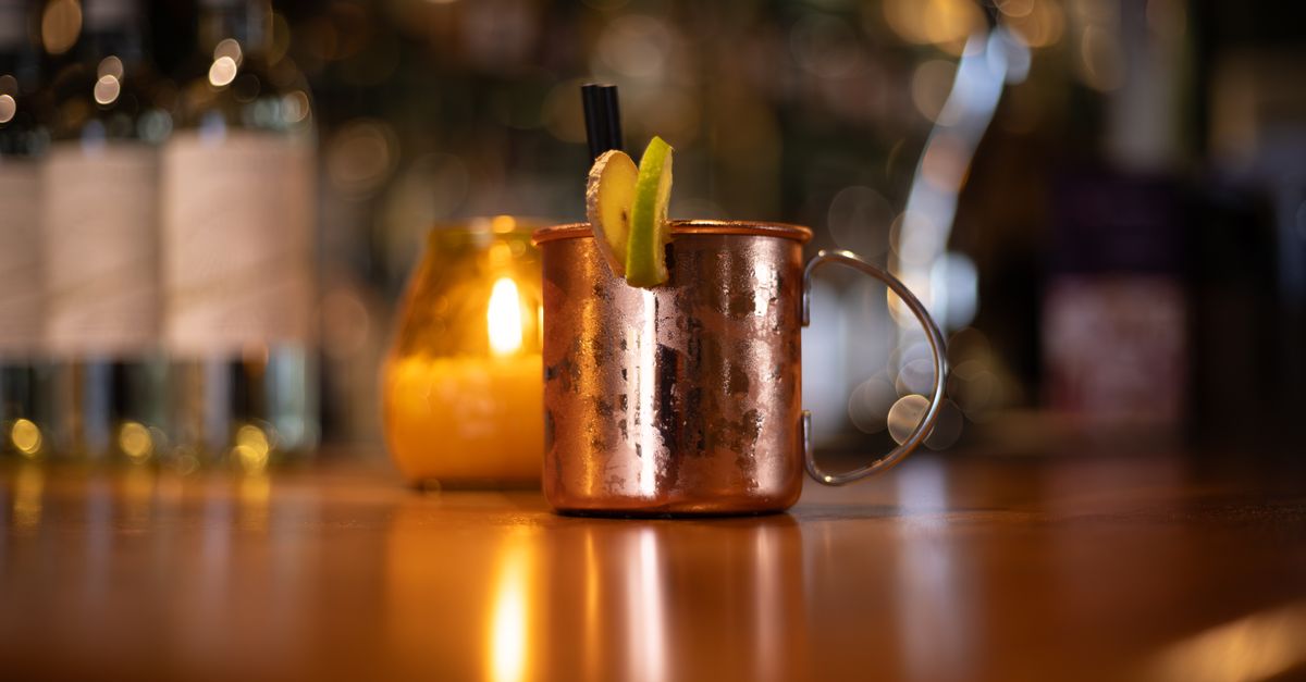 Close-up of a copper mug with a refreshing cocktail garnished with lime on a bar counter.