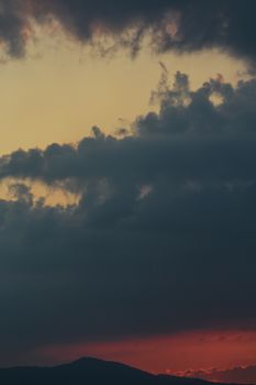 A stunning view of dark clouds against a colorful sunset sky over silhouetted mountains.