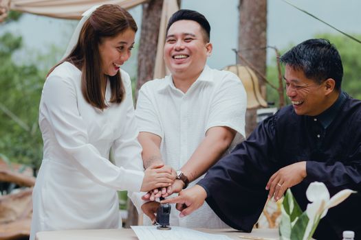 Happy couple with registrar stamping wedding document outdoors, celebrating marriage.
