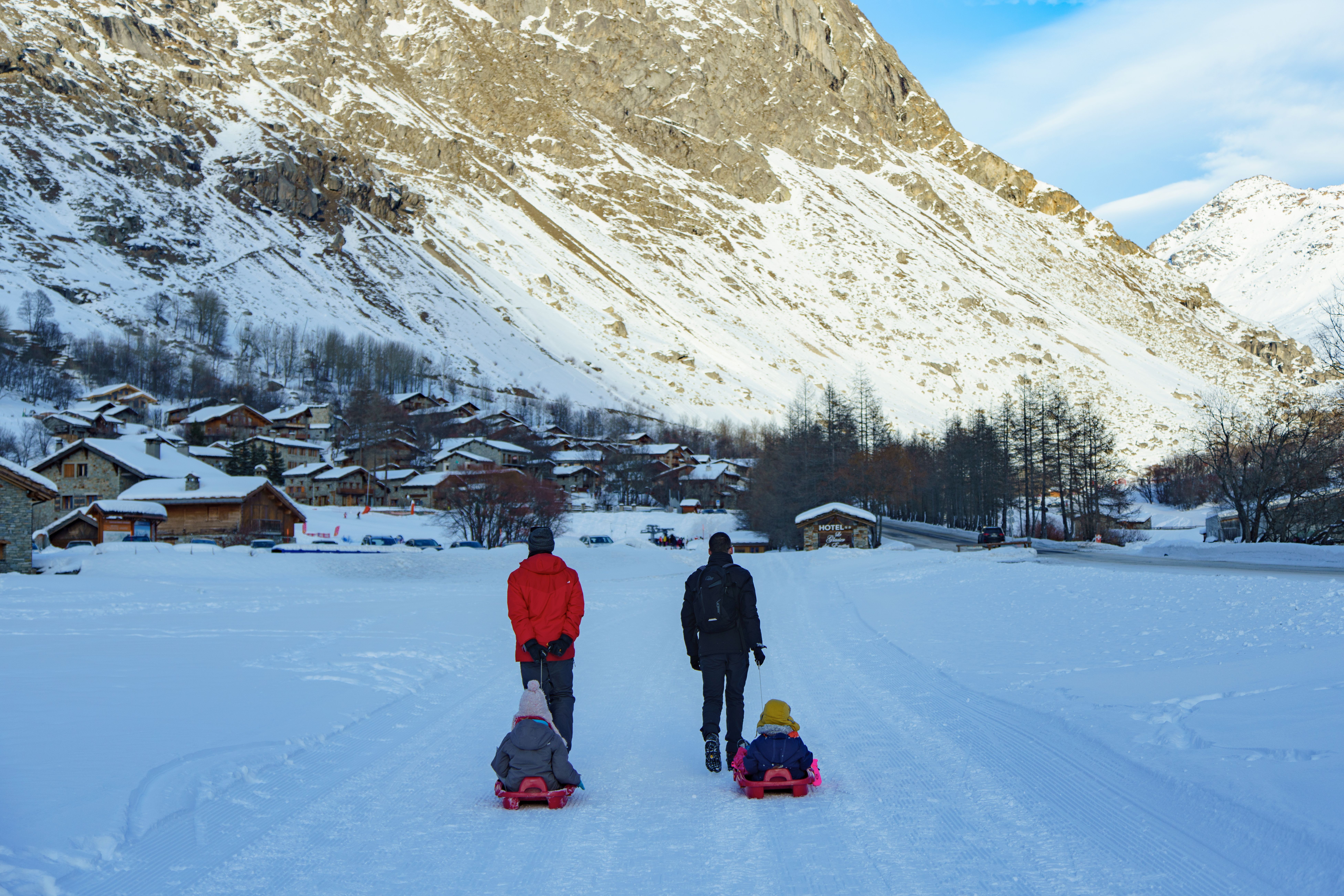 Família se diverte andando de trenó em Snowmass Village, com montanhas nevadas ao fundo. Perfeita para férias em família.