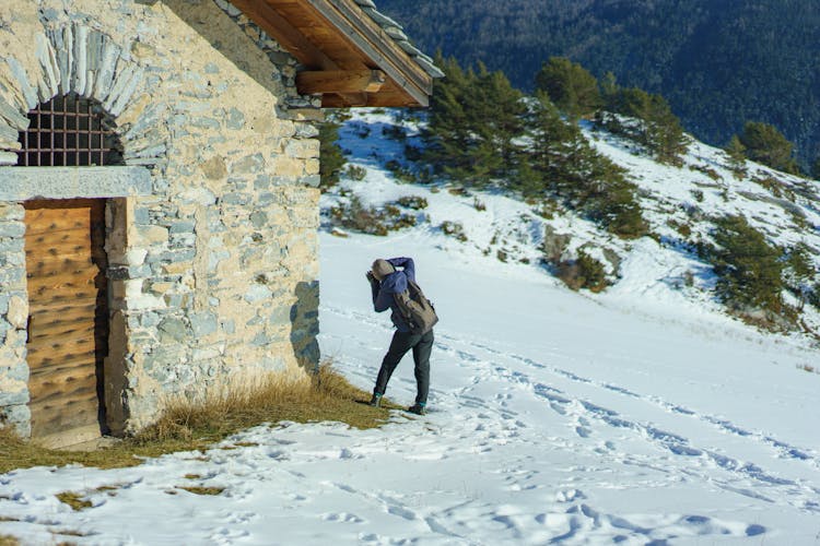 Hiking Woman Standing By Stone Building On Trail In Winter