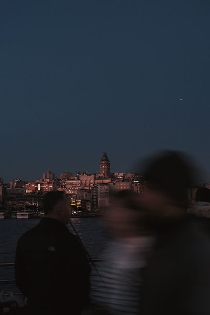 Blurred silhouettes of people with Galata Tower in the background at night in Istanbul.