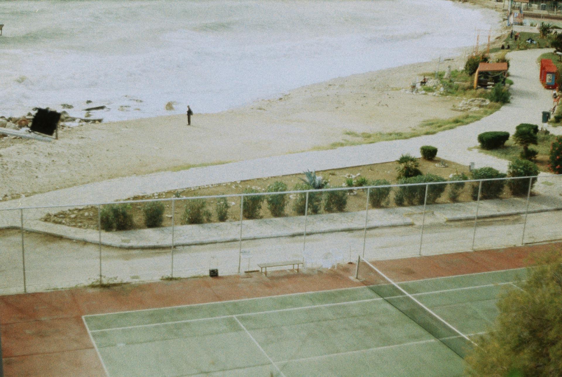 A tranquil view of a tennis court by the beach in Piraeus, Greece, showcasing a calm coastal scene.