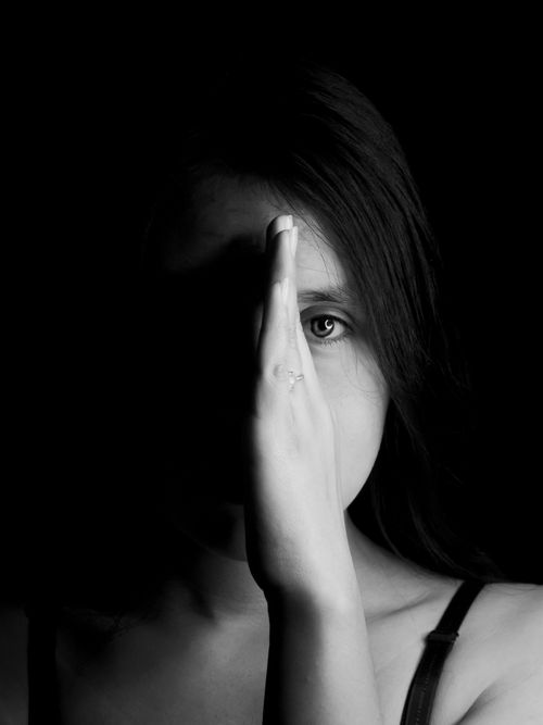 Free An intense black and white portrait of a woman with a hand obscuring half of her face, creating a shadow effect. Stock Photo
